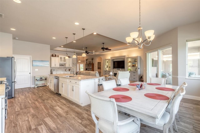 dining room with a raised ceiling, ceiling fan with notable chandelier, light hardwood / wood-style flooring, and sink