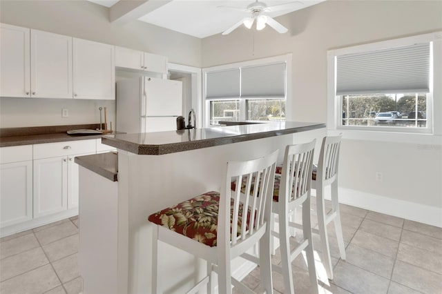 kitchen featuring a breakfast bar, ceiling fan, light tile patterned floors, white refrigerator, and white cabinetry