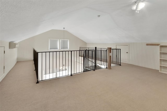 additional living space with light carpet, a textured ceiling, vaulted ceiling, and an AC wall unit