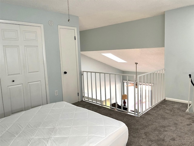 bedroom with a closet, dark carpet, a textured ceiling, and vaulted ceiling with skylight