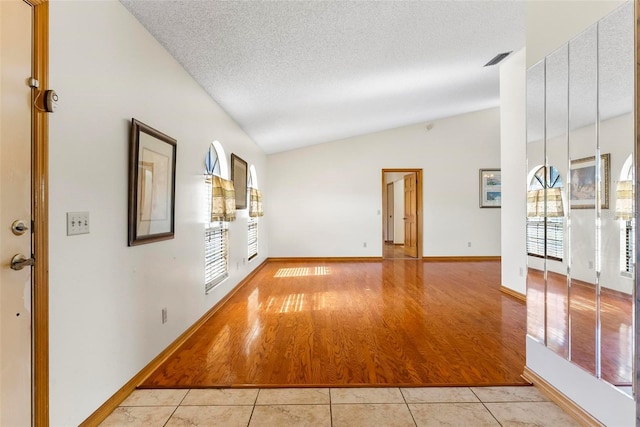 unfurnished room with a textured ceiling, plenty of natural light, light hardwood / wood-style floors, and vaulted ceiling