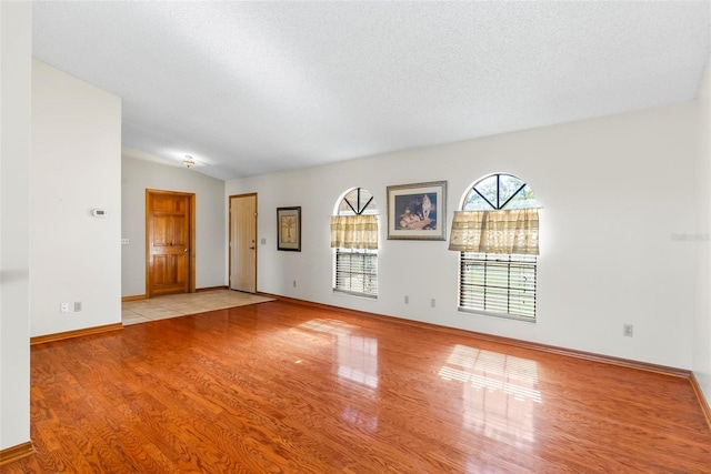 spare room with vaulted ceiling, a textured ceiling, and light hardwood / wood-style flooring