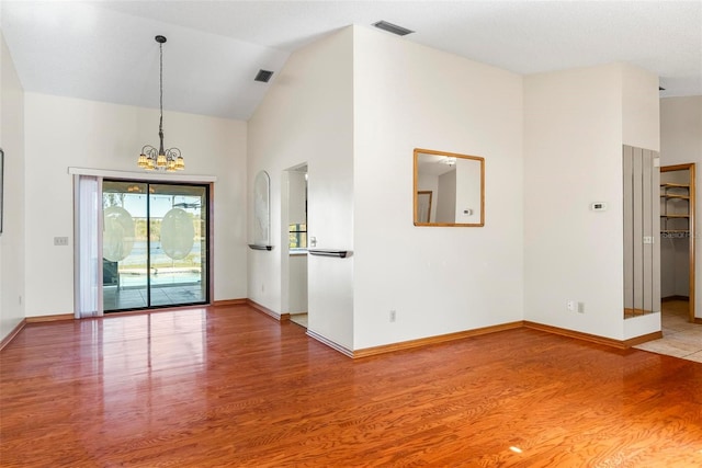 empty room featuring hardwood / wood-style flooring, a notable chandelier, and high vaulted ceiling