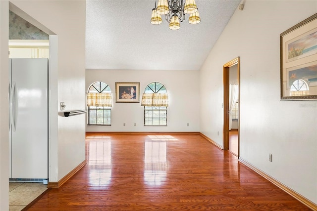 unfurnished living room featuring a chandelier, hardwood / wood-style floors, a textured ceiling, and vaulted ceiling