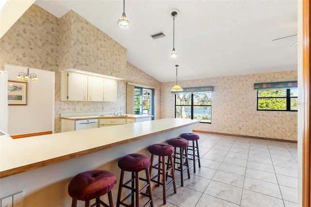 kitchen featuring dishwasher, a kitchen breakfast bar, a notable chandelier, decorative light fixtures, and cream cabinetry