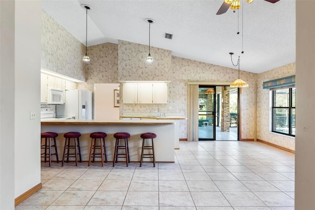 kitchen with a kitchen bar, kitchen peninsula, ceiling fan, and white appliances