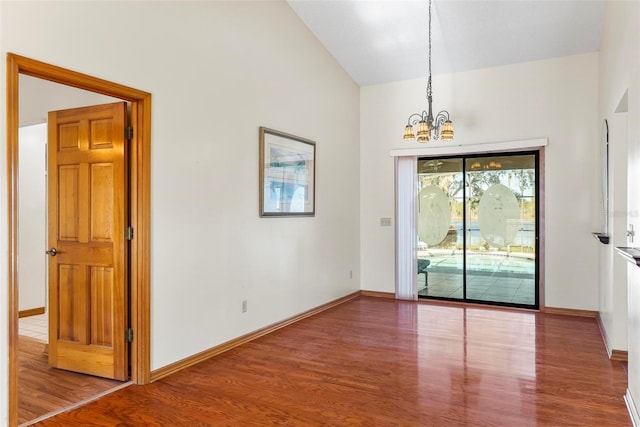 empty room with vaulted ceiling, hardwood / wood-style flooring, and an inviting chandelier