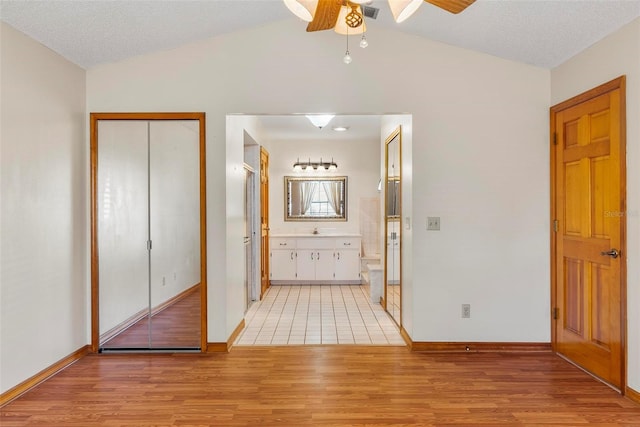 corridor with a textured ceiling, lofted ceiling, and light wood-type flooring