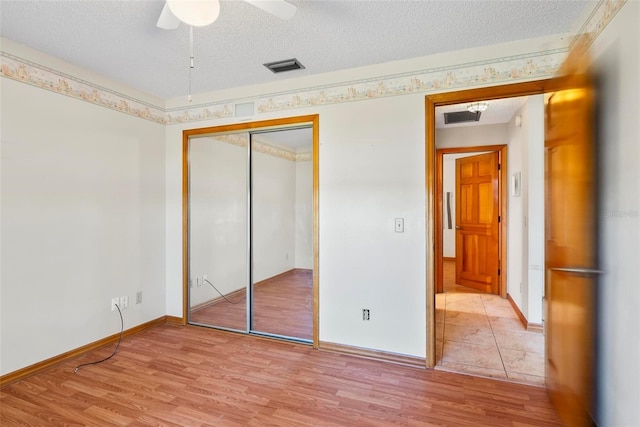 unfurnished bedroom featuring ceiling fan, a closet, a textured ceiling, and light hardwood / wood-style flooring