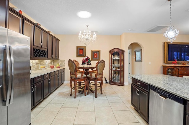 kitchen featuring decorative light fixtures, light stone counters, dark brown cabinets, and stainless steel appliances