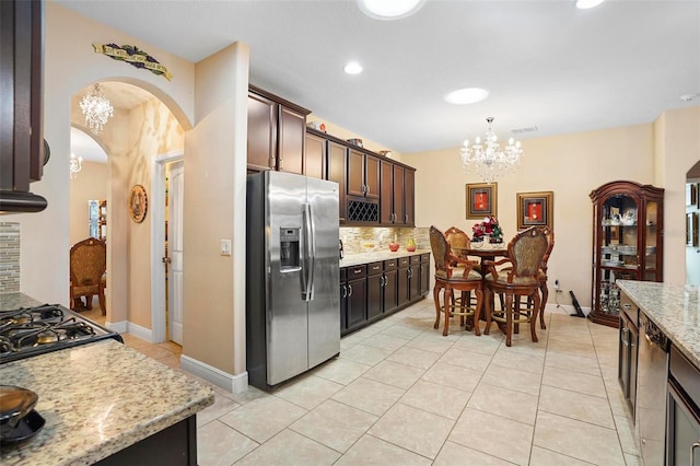 kitchen with light tile patterned floors, light stone countertops, appliances with stainless steel finishes, dark brown cabinets, and a chandelier