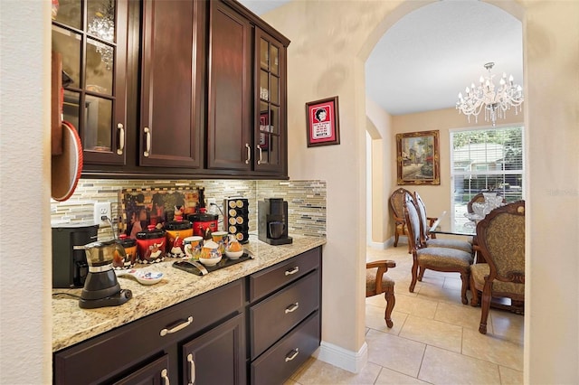 bar with dark brown cabinetry, backsplash, hanging light fixtures, and a chandelier