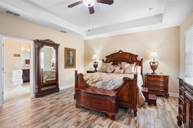 bedroom with a tray ceiling, connected bathroom, ceiling fan, and light wood-type flooring