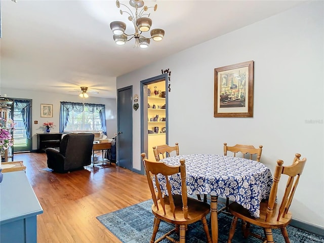 dining space with ceiling fan with notable chandelier and wood-type flooring