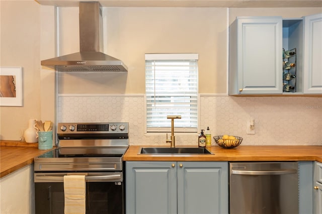 kitchen featuring backsplash, appliances with stainless steel finishes, wall chimney range hood, and wood counters