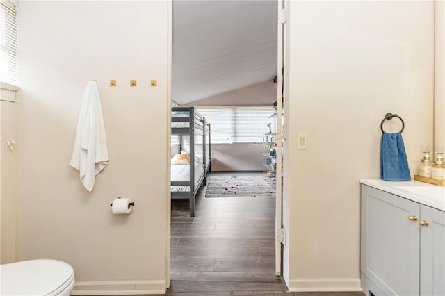 bathroom with hardwood / wood-style floors, vanity, toilet, and vaulted ceiling