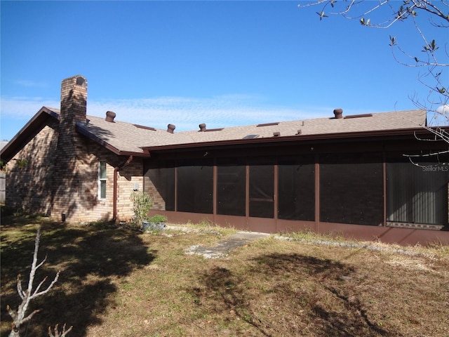 back of property featuring a shingled roof, a chimney, a yard, and a sunroom