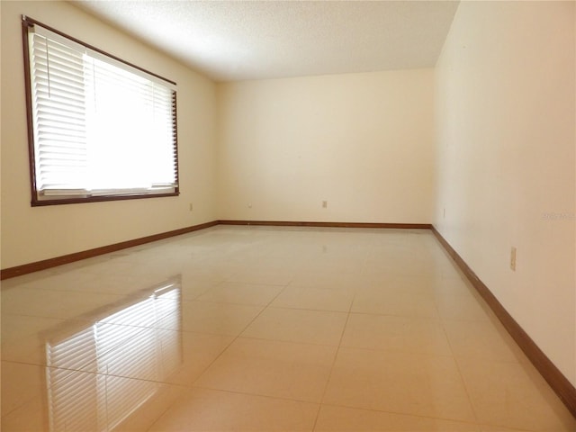 empty room with light tile patterned floors, a textured ceiling, and baseboards