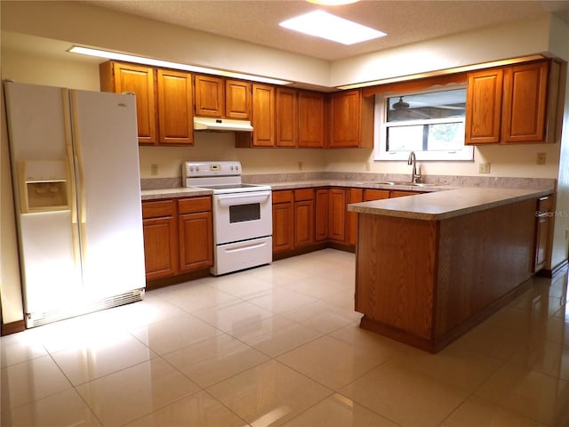 kitchen featuring a sink, under cabinet range hood, white appliances, a peninsula, and brown cabinetry