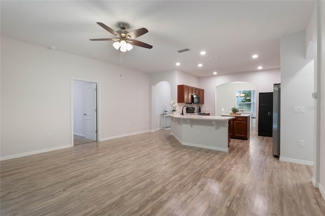 kitchen with light wood-type flooring, ceiling fan, sink, black appliances, and a breakfast bar area