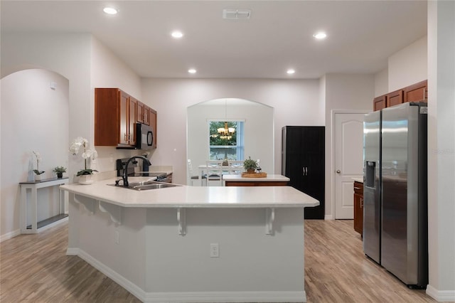 kitchen with stainless steel fridge with ice dispenser, arched walkways, a peninsula, and brown cabinetry
