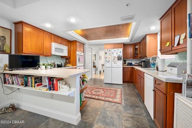 kitchen featuring white appliances, sink, decorative backsplash, a tray ceiling, and kitchen peninsula