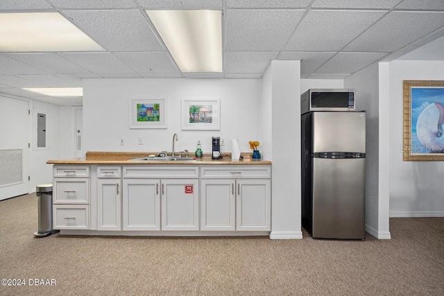 kitchen with a drop ceiling, light carpet, white cabinets, sink, and appliances with stainless steel finishes