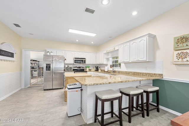 kitchen with a breakfast bar, appliances with stainless steel finishes, kitchen peninsula, light stone countertops, and white cabinets