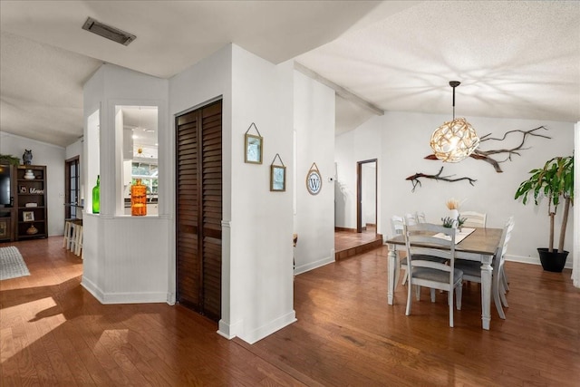 dining area featuring a chandelier, a textured ceiling, dark hardwood / wood-style floors, and vaulted ceiling