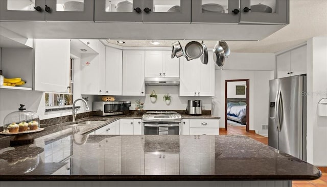 kitchen with dark stone counters, white cabinets, sink, appliances with stainless steel finishes, and kitchen peninsula