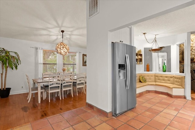 kitchen with stainless steel refrigerator with ice dispenser, a textured ceiling, decorative light fixtures, a chandelier, and light hardwood / wood-style floors