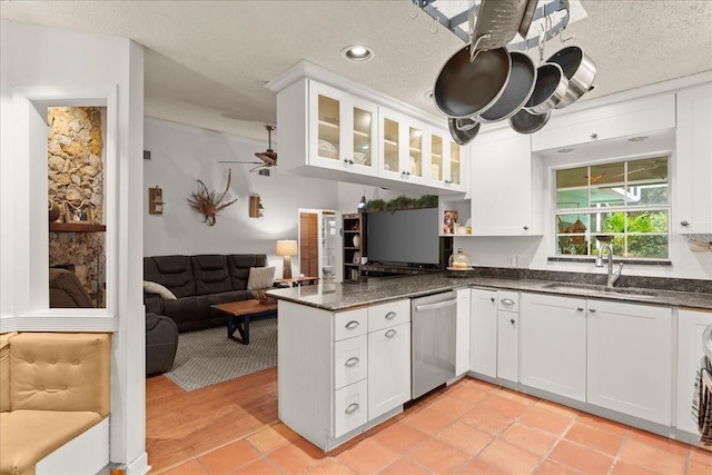 kitchen featuring white cabinets, stainless steel dishwasher, dark stone counters, and sink