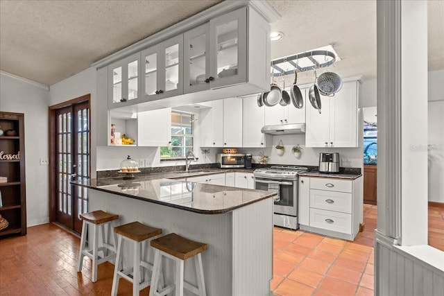 kitchen featuring kitchen peninsula, stainless steel gas stove, white cabinets, and sink