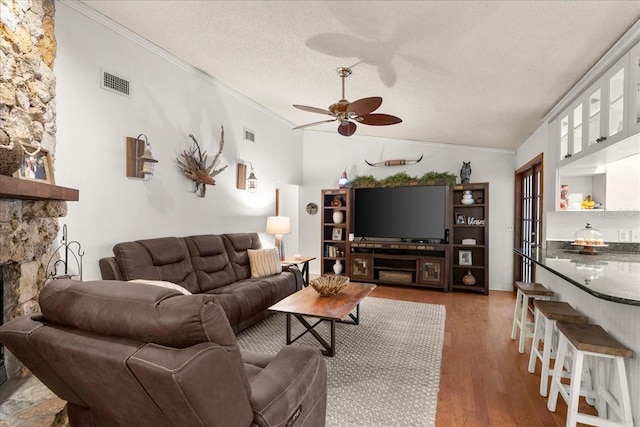 living room featuring a textured ceiling, vaulted ceiling, ceiling fan, crown molding, and hardwood / wood-style flooring