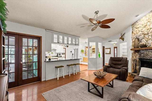 living room with french doors, light wood-type flooring, a textured ceiling, ceiling fan, and a fireplace