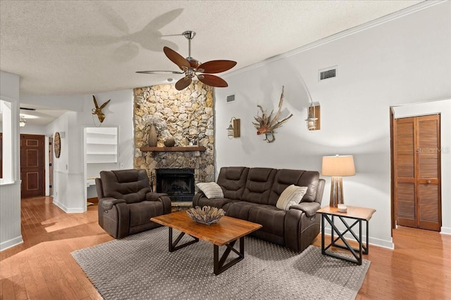 living room featuring a textured ceiling, light hardwood / wood-style floors, a stone fireplace, and ceiling fan