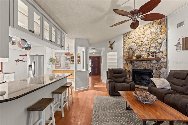 living room featuring a fireplace, ceiling fan, light wood-type flooring, and a textured ceiling