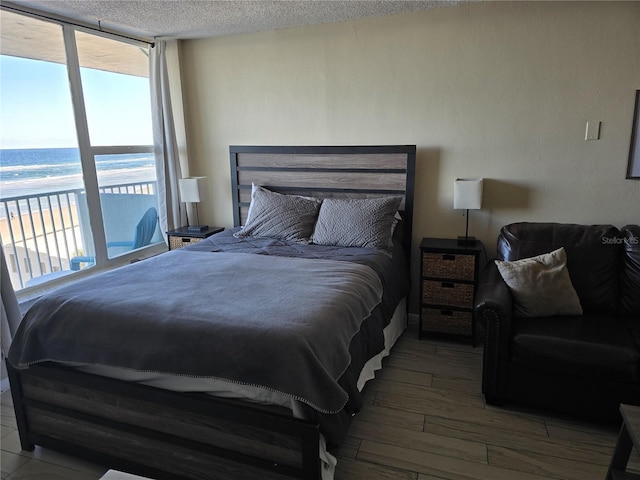 bedroom featuring hardwood / wood-style floors, a textured ceiling, a water view, and access to outside