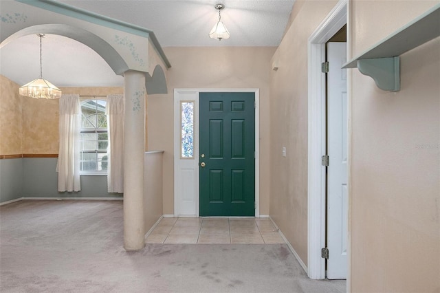 foyer entrance with ornate columns, light carpet, a textured ceiling, and a notable chandelier