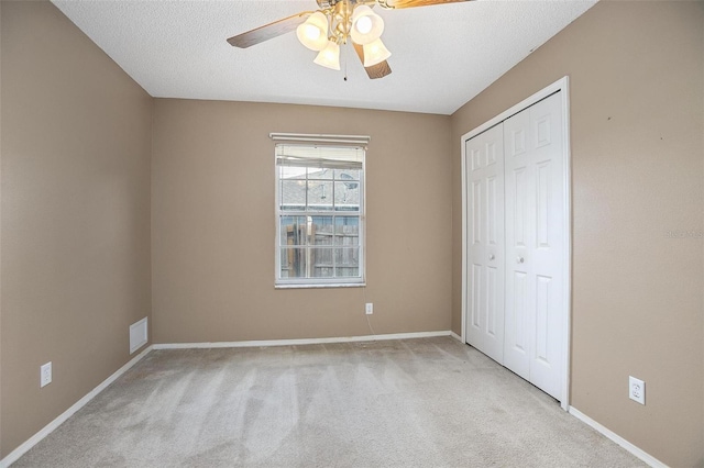 unfurnished bedroom featuring light carpet, a textured ceiling, a closet, and ceiling fan