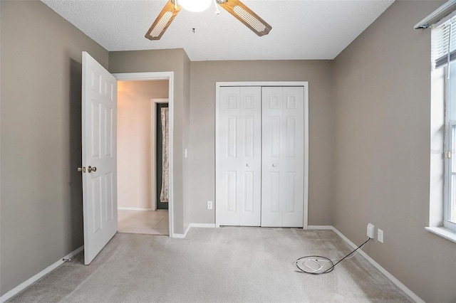 unfurnished bedroom with a textured ceiling, a closet, ceiling fan, and light colored carpet