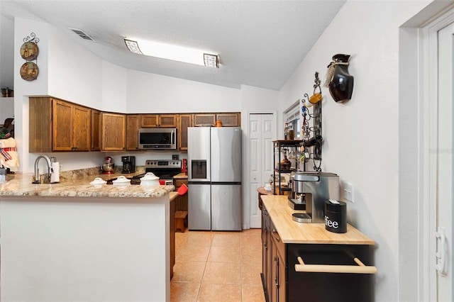 kitchen with vaulted ceiling, a textured ceiling, appliances with stainless steel finishes, light tile patterned flooring, and kitchen peninsula