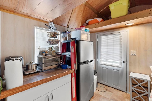 kitchen featuring wooden walls, light tile patterned floors, white cabinetry, stainless steel refrigerator, and tile counters