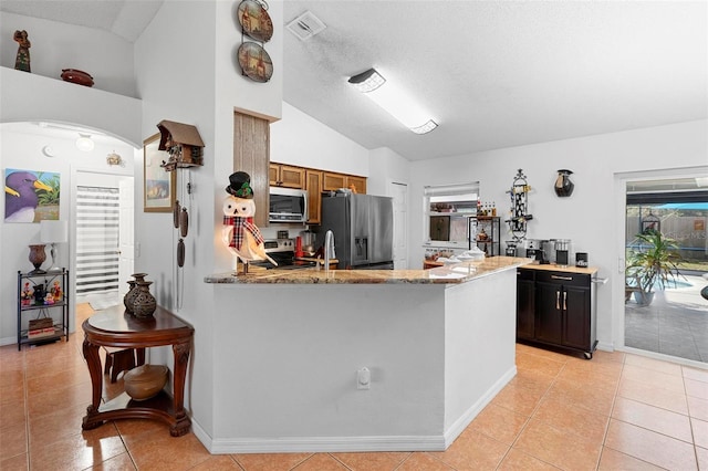 kitchen featuring light stone counters, kitchen peninsula, lofted ceiling, light tile patterned floors, and appliances with stainless steel finishes