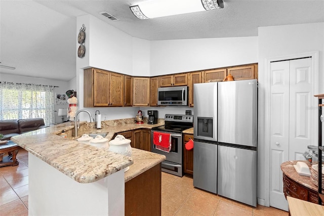 kitchen with high vaulted ceiling, light tile patterned floors, kitchen peninsula, and appliances with stainless steel finishes