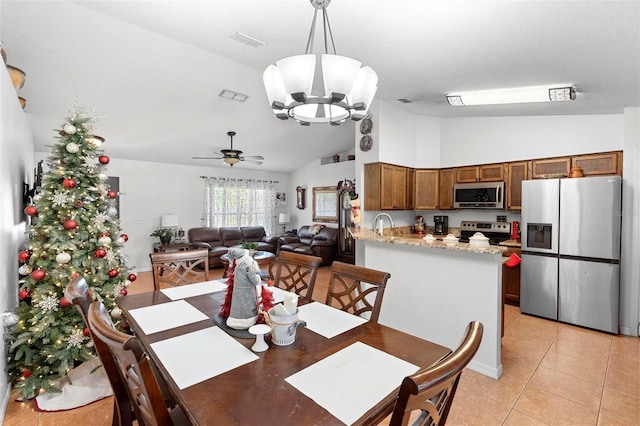 dining space with sink, light tile patterned flooring, ceiling fan with notable chandelier, and high vaulted ceiling