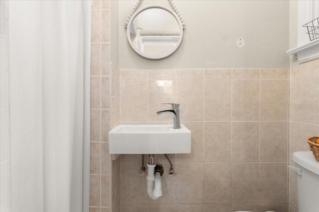 bathroom featuring toilet, tile walls, and sink