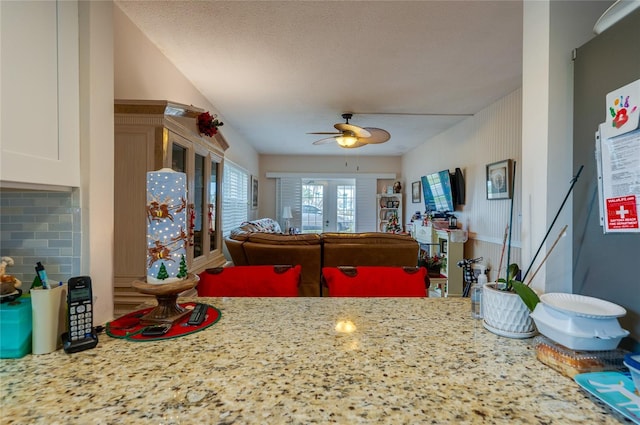 kitchen with ceiling fan, backsplash, light stone countertops, white cabinets, and french doors