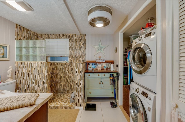 laundry area with stacked washer and dryer, light tile patterned floors, and a textured ceiling