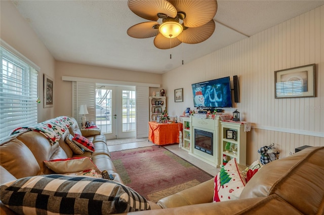 tiled living room with ceiling fan, french doors, and wood walls